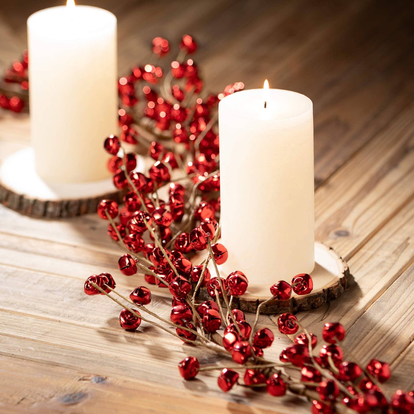 Two white candles on a wooden surface with red jingle bell garland