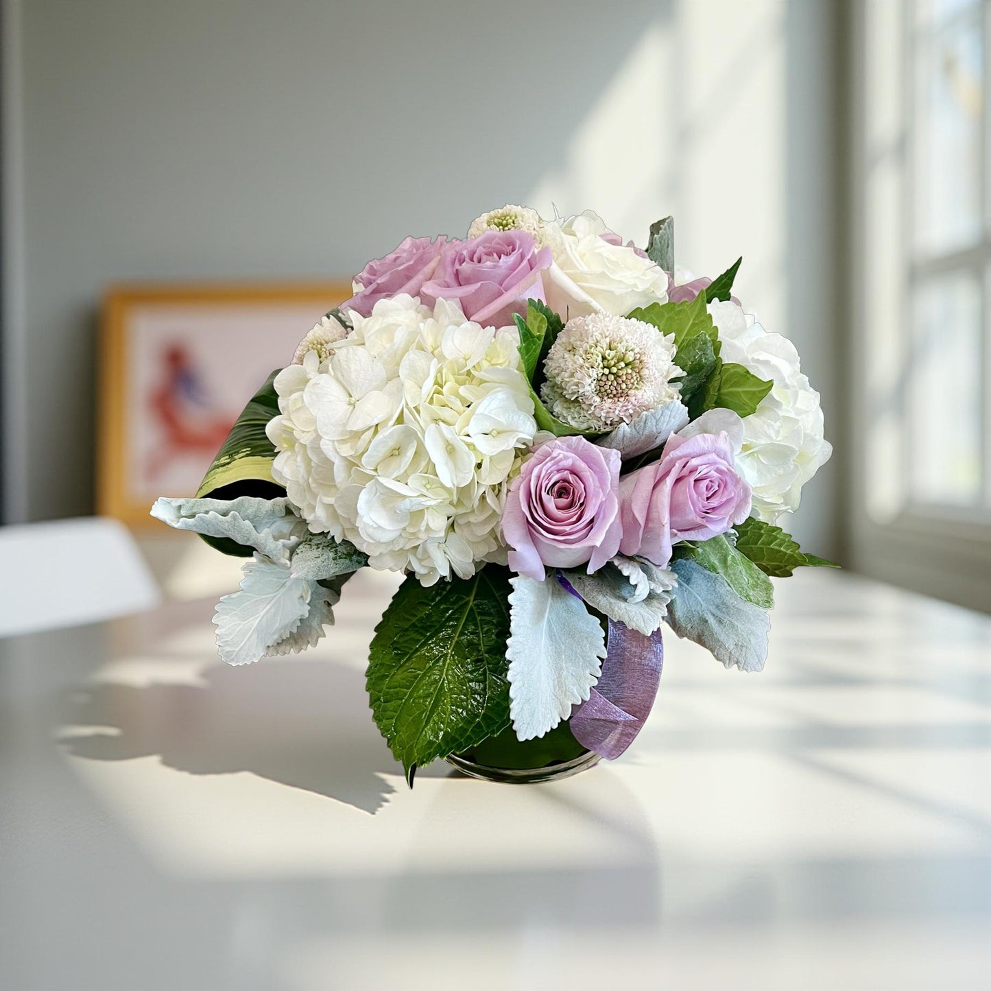 white hydrangea, purple roses and greenery in a low and lush flower arrangement