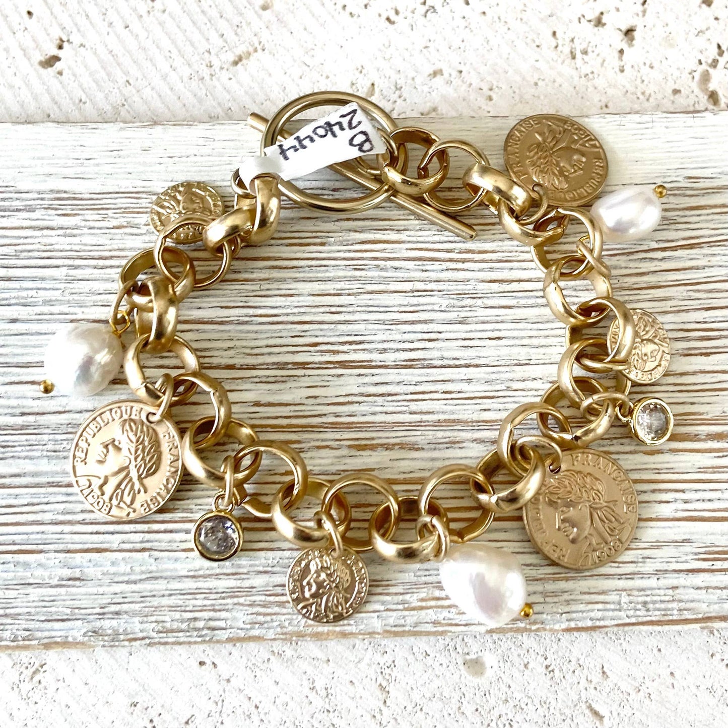 Gold charm bracelet with coins and pearls on a wooden surface