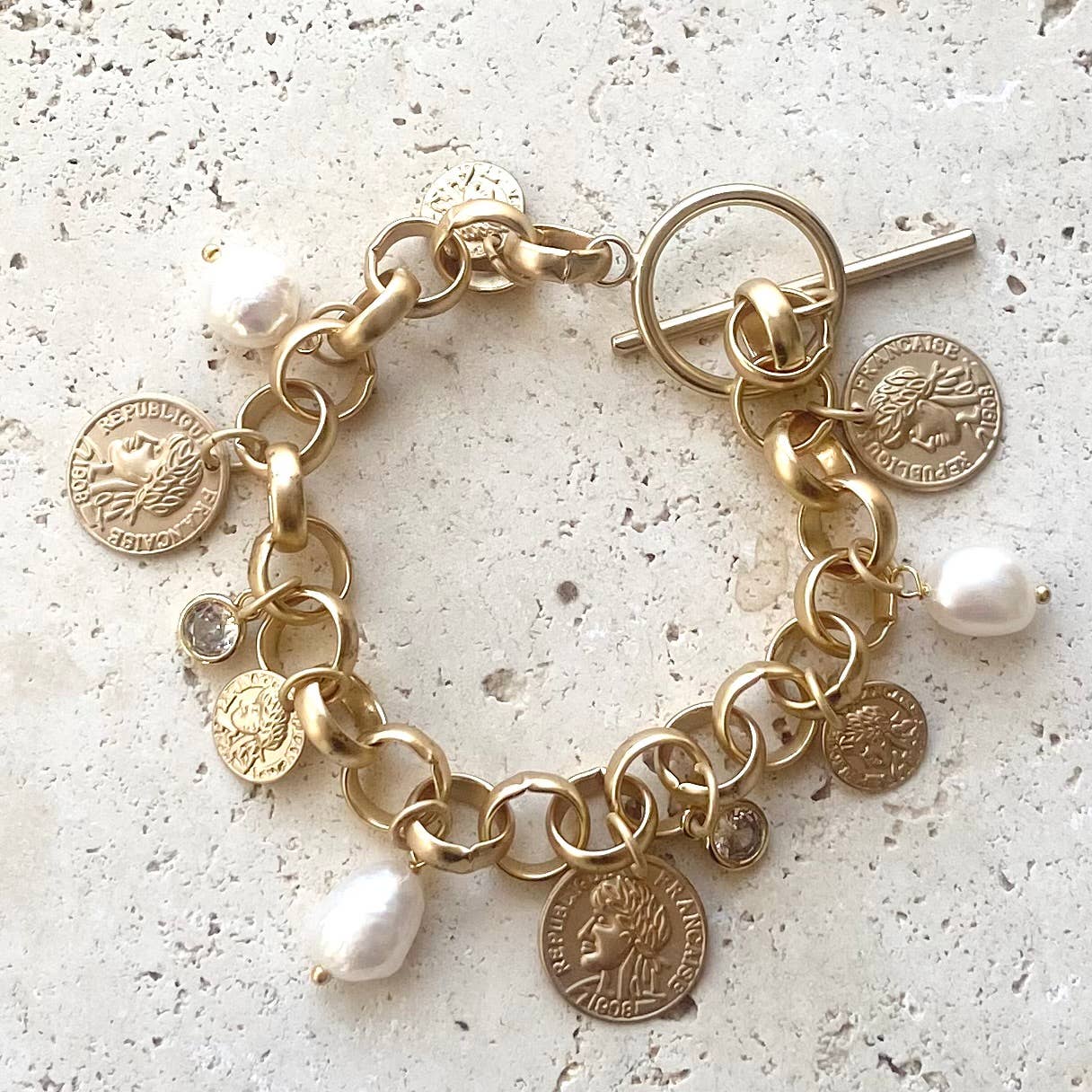 Gold charm bracelet with coins and pearls on a light background