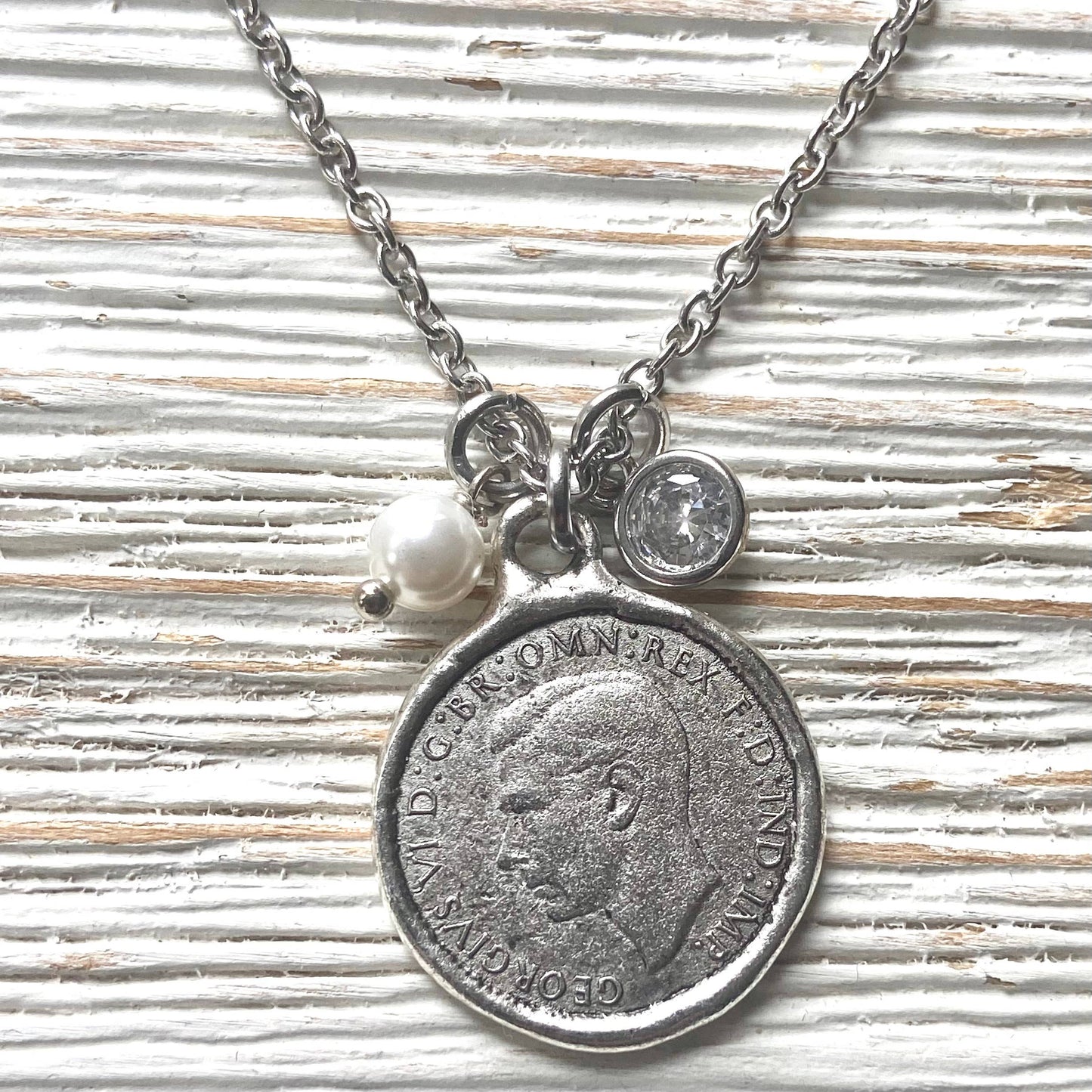 Necklace with vintage coin pendant and pearl charm on a textured surface
