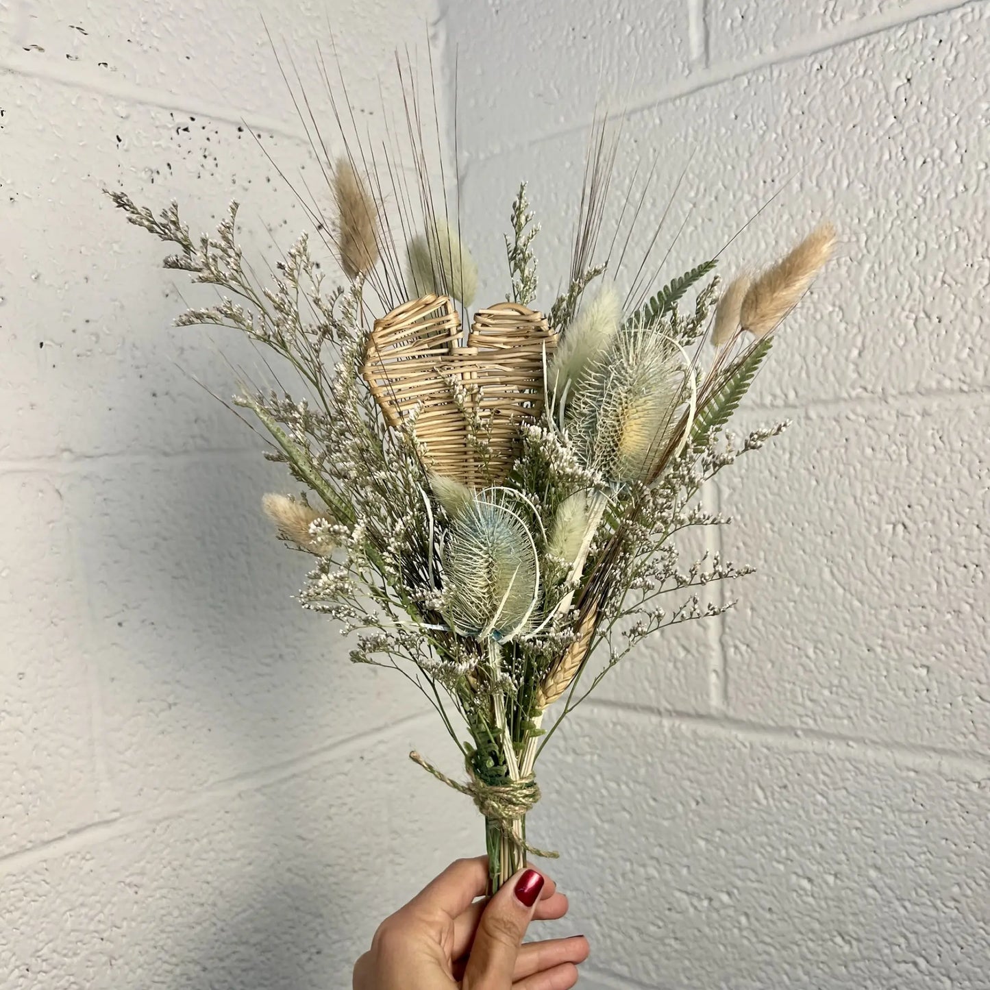 Bouquet of dried flowers held against a white brick wall