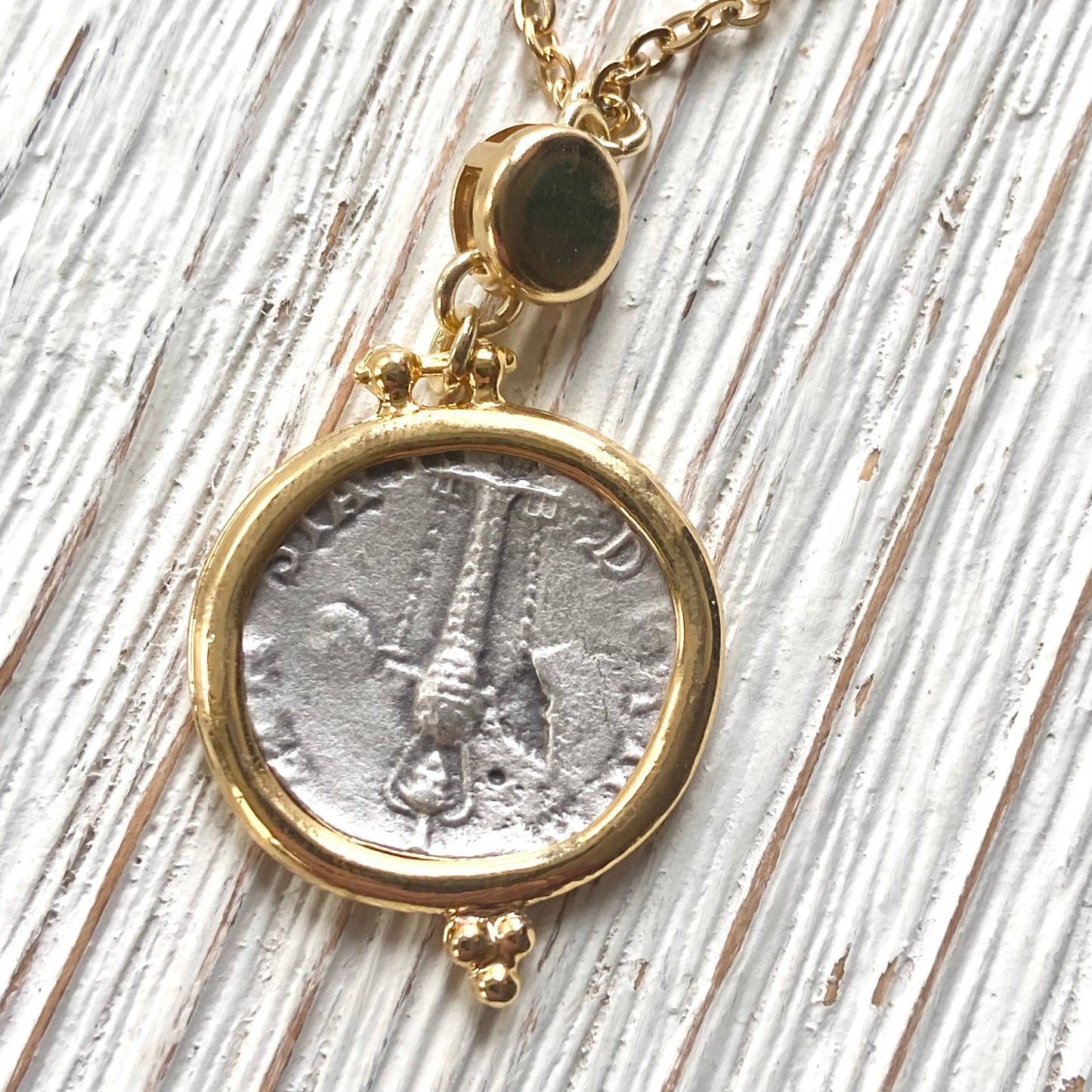 Gold necklace with a pendant featuring a silver coin on a wooden surface