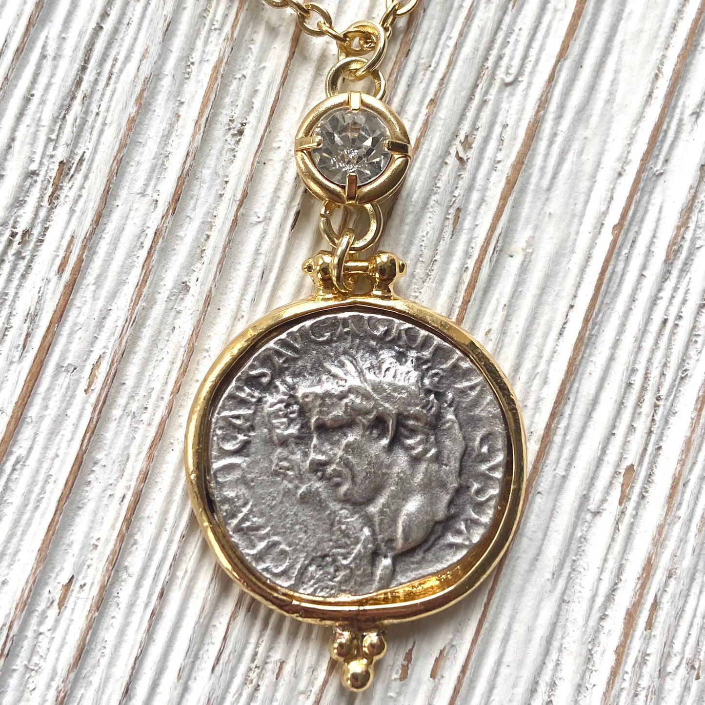 Necklace with a gold and silver coin pendant on a wooden surface