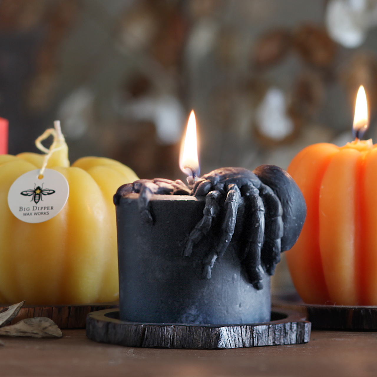 Candle with a spider design in front of pumpkins