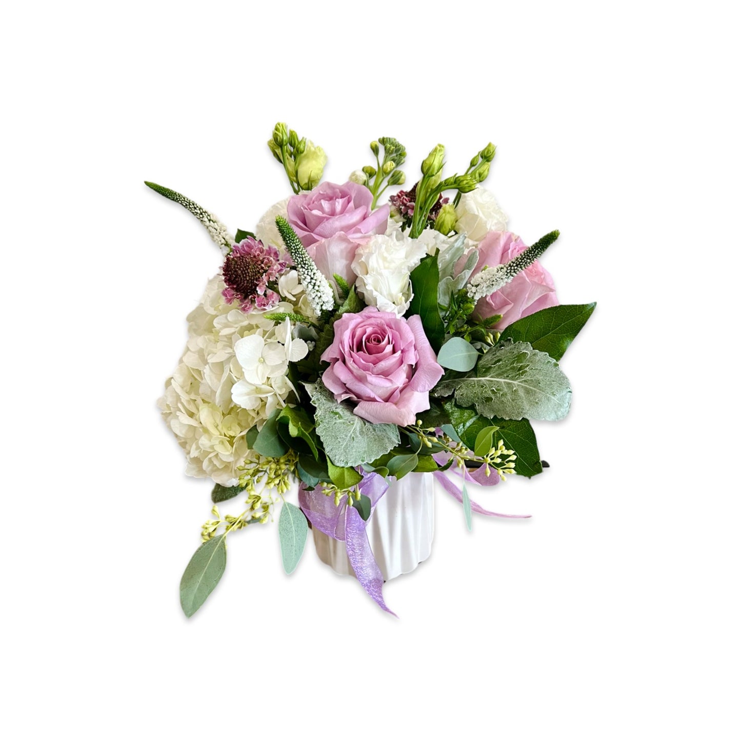 A fresh flower arrangement featuring a mix of white, cream, and purple flowers, with green foliage and pink accents, presented in a white vase.