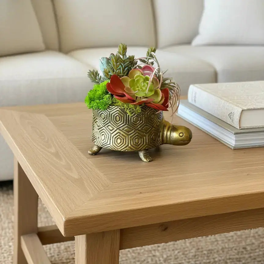 Decorative turtle planter with flowers on a wooden coffee table in a living room.