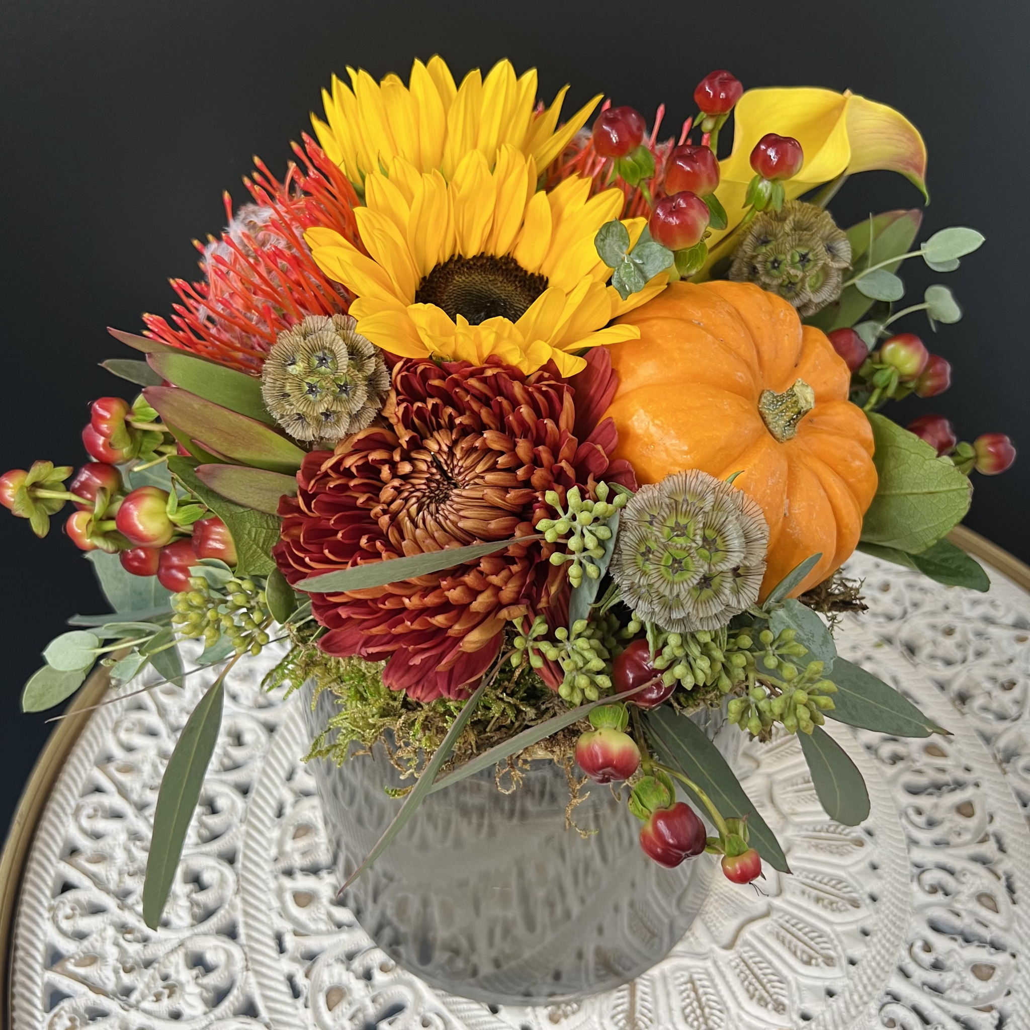 A vibrant floral arrangement featuring sunflowers, pumpkins, and various other autumn-colored flowers in a modern metal container. Las Vegas delivery available