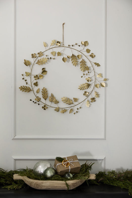 Decorative wreath with gold leaves on a white wall, with a small gift and greenery below.