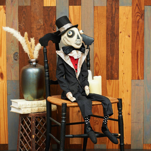 Joe Spencer skeleton doll in a suit sitting on a chair against a wooden paneled wall.