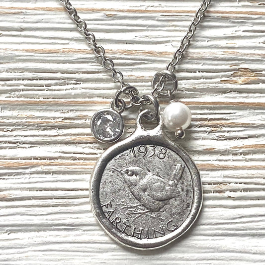 Necklace with a coin pendant featuring the year 1938 and a pearl charm on a textured surface.