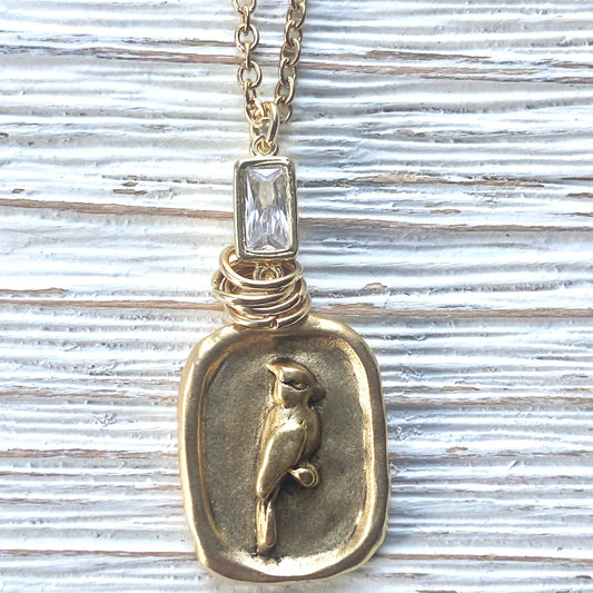 Gold pendant necklace with bird design on a textured surface