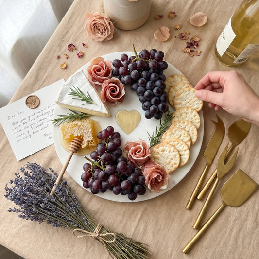 Platter of assorted cheeses, crackers, and grapes with a hand reaching for a cracker on a wooden table.