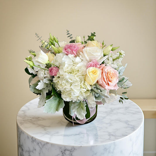 white, pink, yellow roses and hydrangea in a vase on a marble table