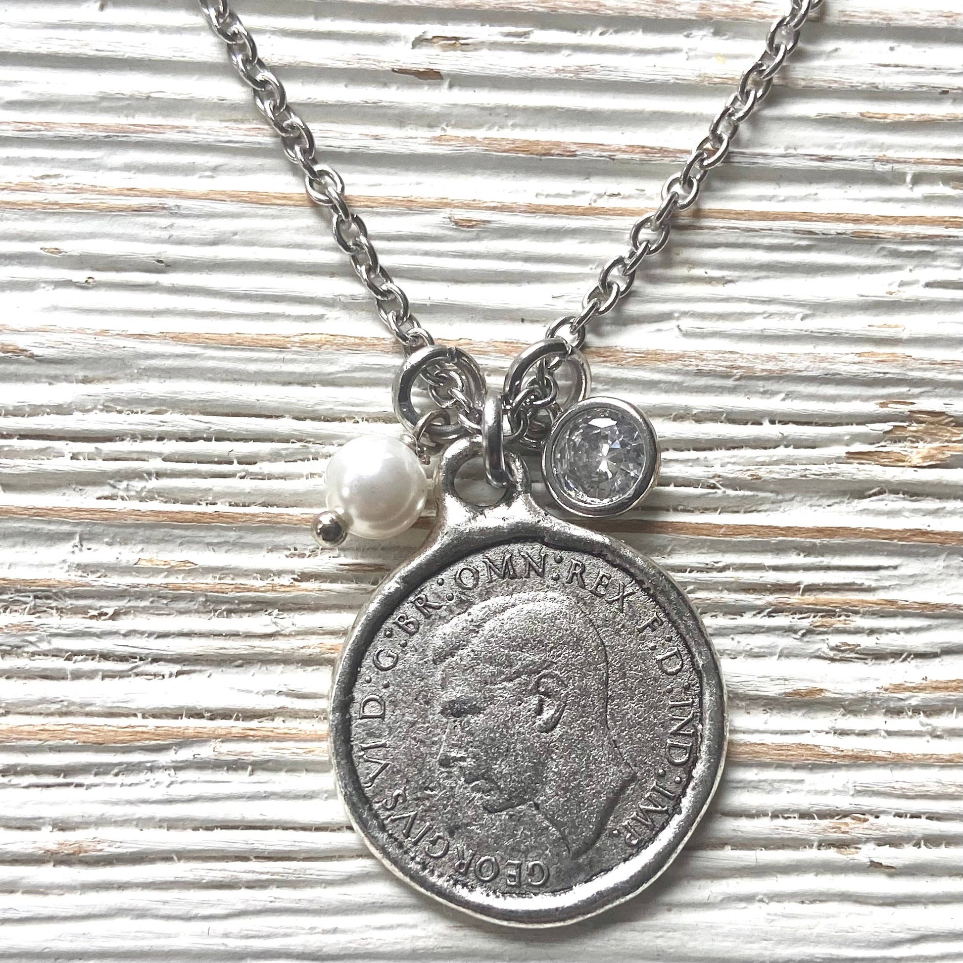 Necklace with vintage coin pendant and pearl charm on a textured surface