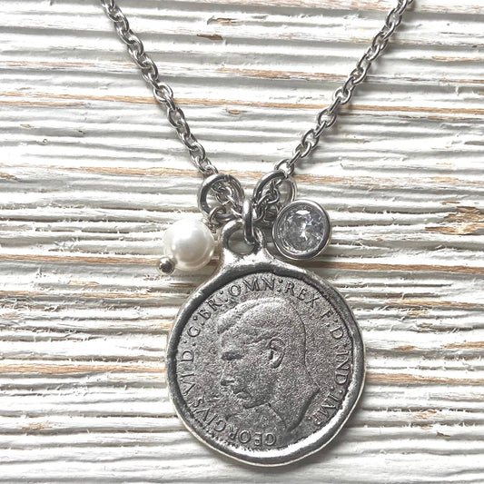 Necklace with vintage coin pendant and pearl charm on a textured surface