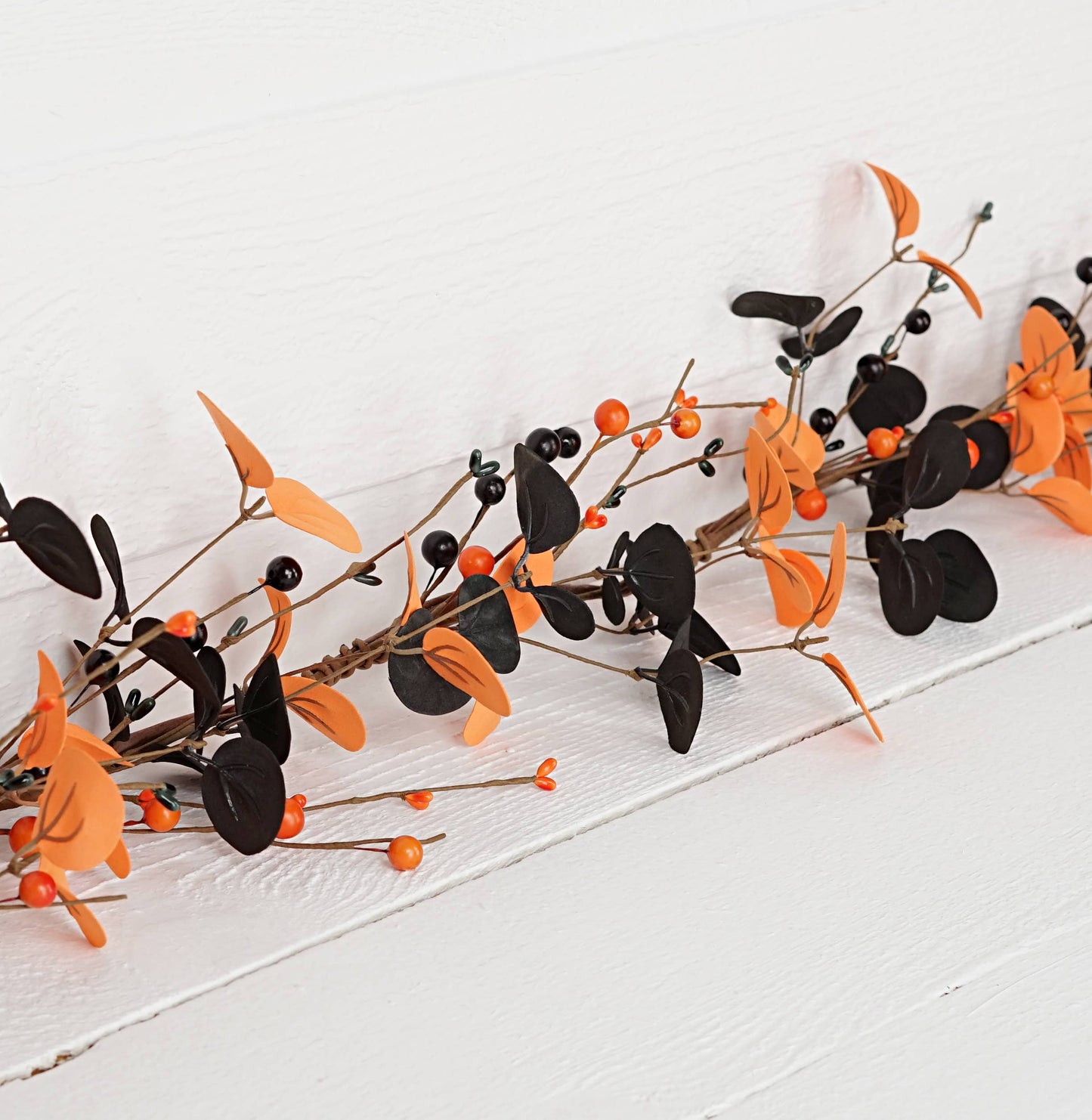 Decorative garland with orange and black leaves on a white surface