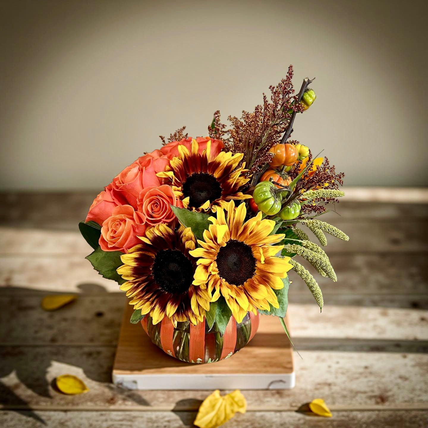 Decorative floral arrangement with sunflowers and roses in a pumpkin container on a wooden surface - Thimbleberry House