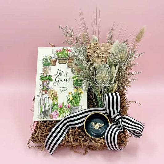 Garden-themed gift set with 'Let it Grow' book, plants, and decorative items on a pink background