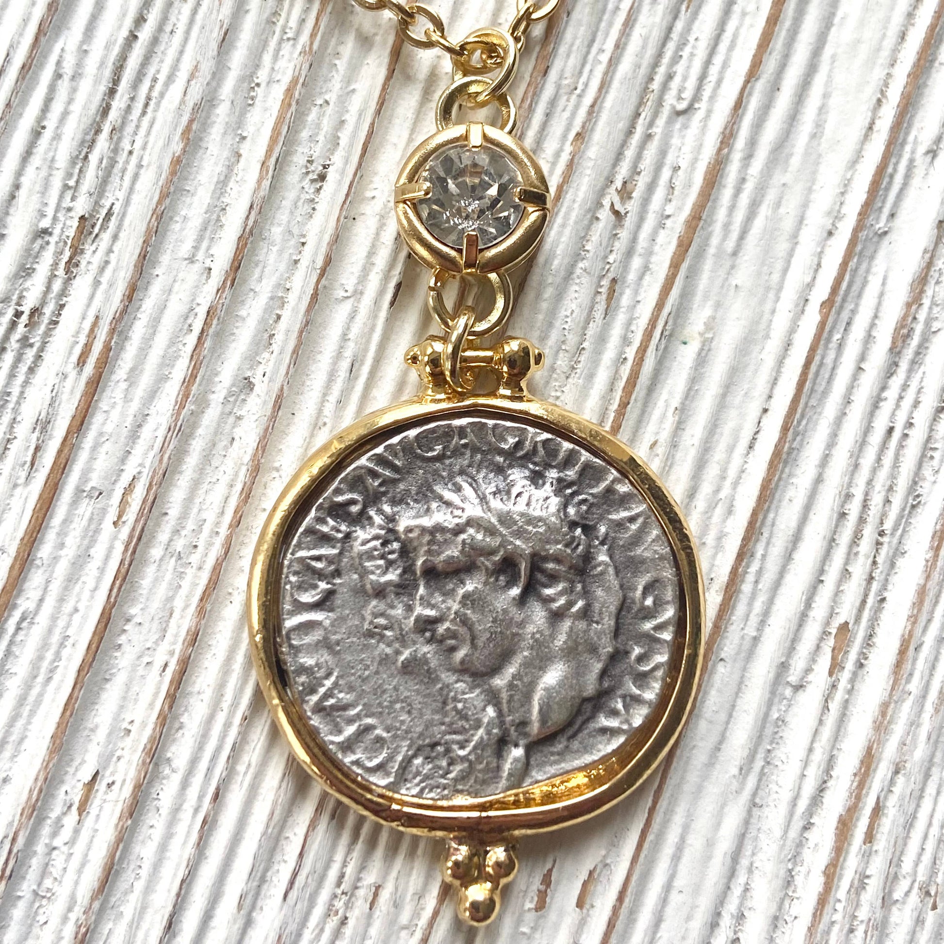 Necklace with a gold and silver coin pendant on a wooden surface
