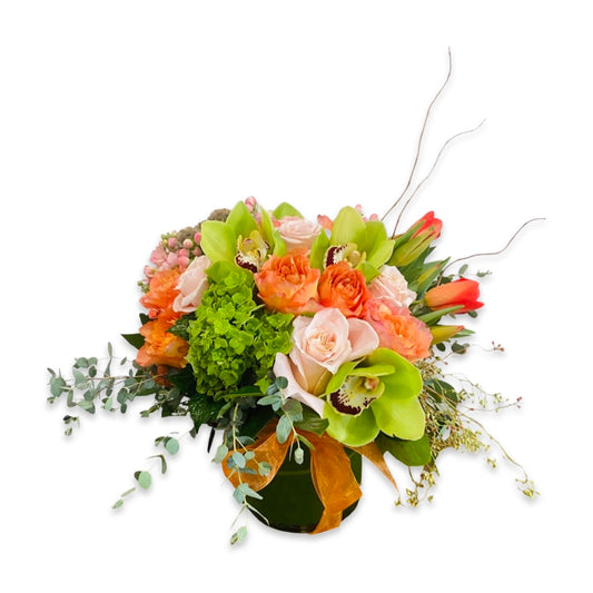 a seasonal mix of peach, orange, and green premium flowers designed and arranged in a glass vase against a white background.