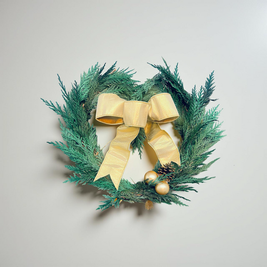Green wreath with a gold bow and ornaments on a light gray background