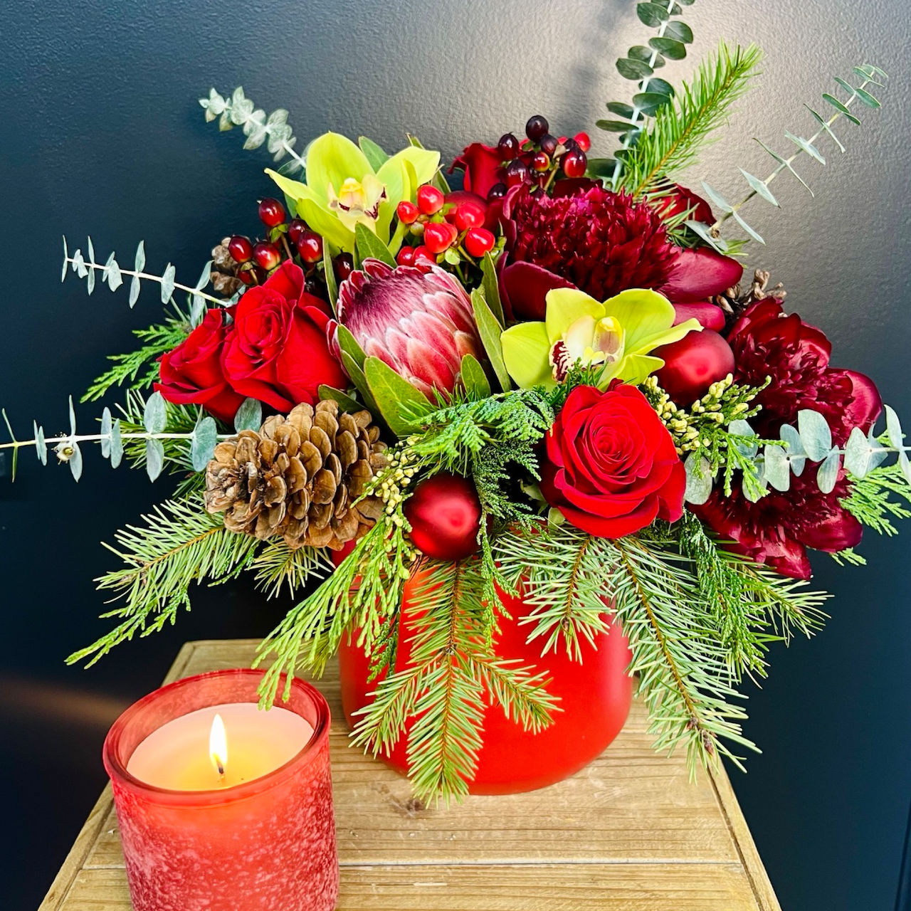 large holiday arrangement on a black background with candle