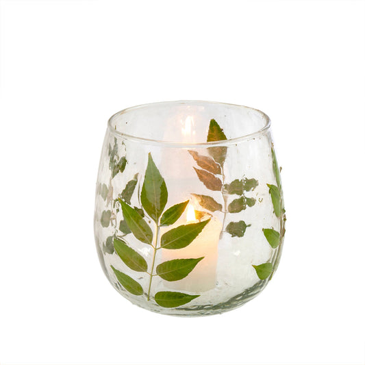 A clear glass votive candle holder with pressed green leaves pattern, containing a lit candle.