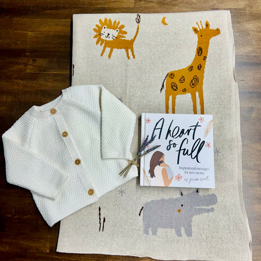 A new baby gift set including a knit cardigan, a baby blanket with animal prints, and a book titled 'A heart so full: Inspirational Messages for New Moms'.