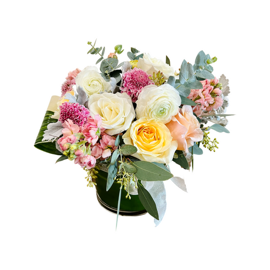 A fresh flower arrangement featuring a variety of soft pastel colored flowers, including white, pink, and yellow blooms, with green leaves and decorative foliage.