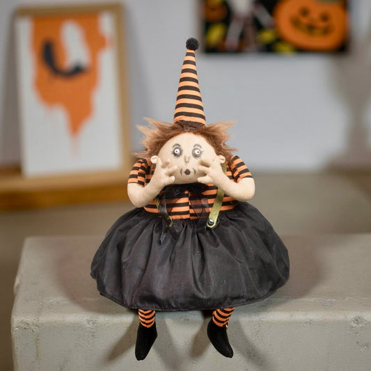 Halloween-themed doll with striped hat and black dress on a concrete surface.