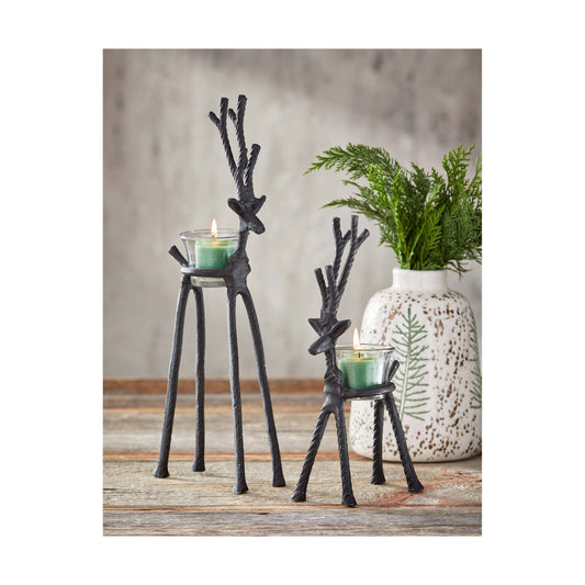 Two black metal deer candle holders with green candles on a wooden surface.