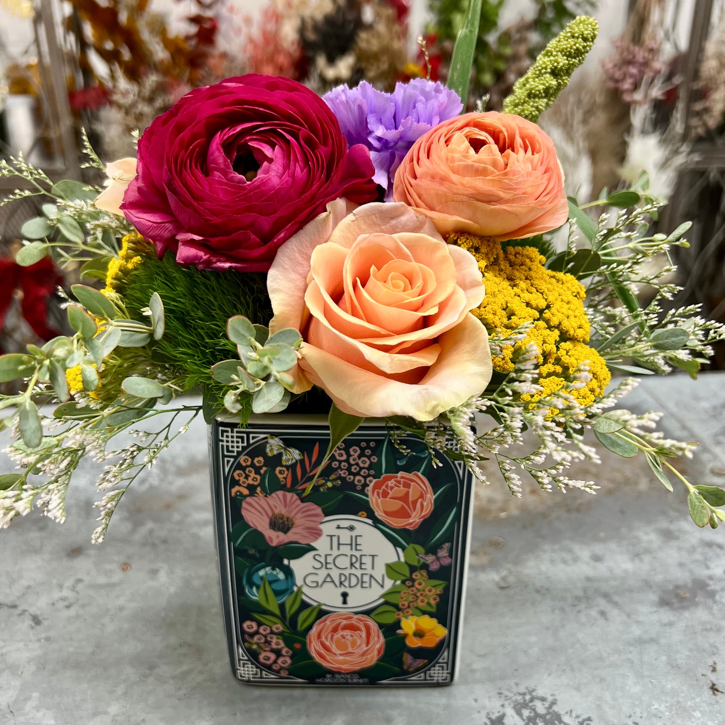 A colorful flower arrangement designed in a ceramic book vase that resembles The Secret Garden
