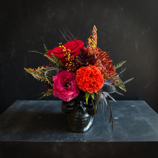 Floral arrangement in a black skull container on a dark surface with a dark background