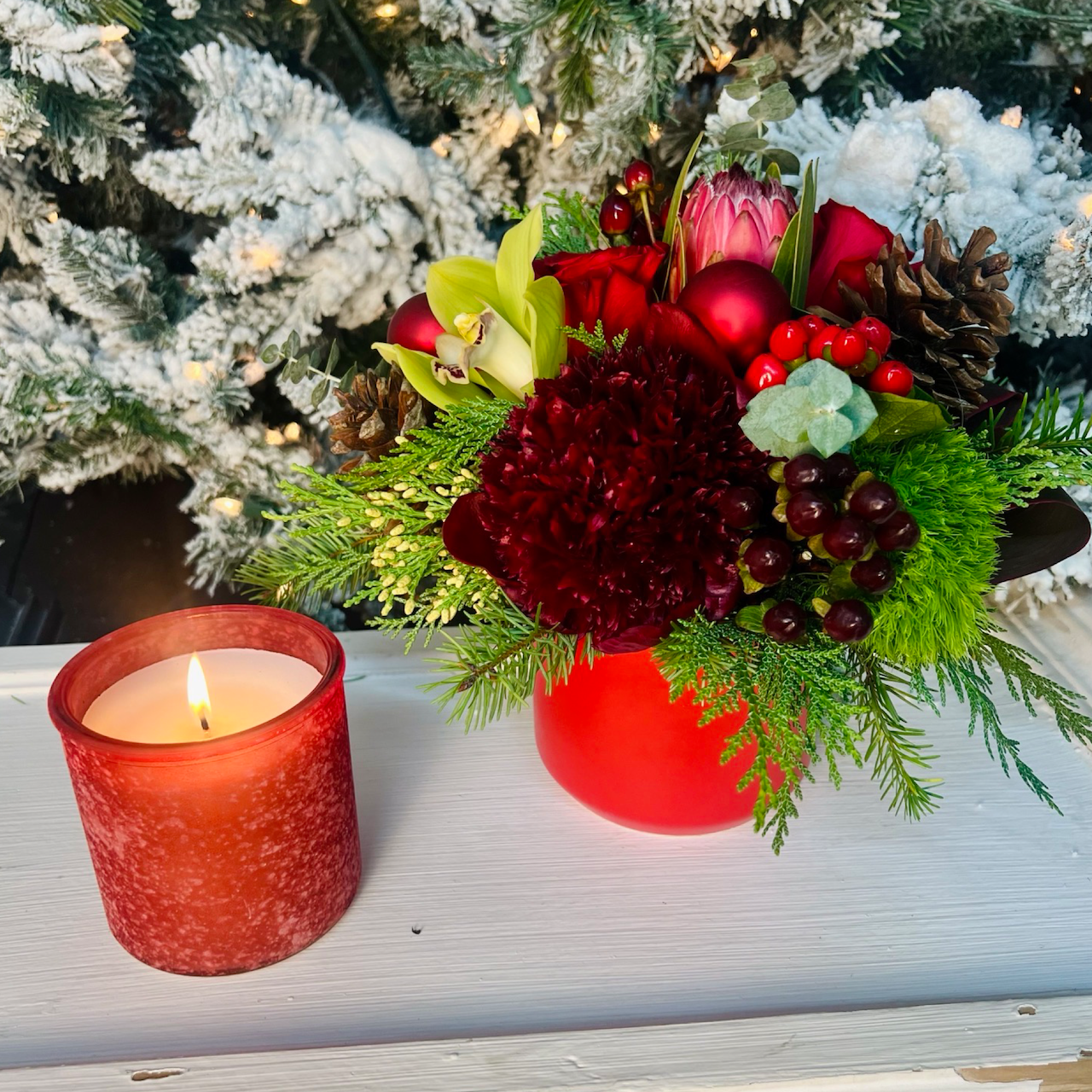 small red holiday arrangement with candle and flocked tree background