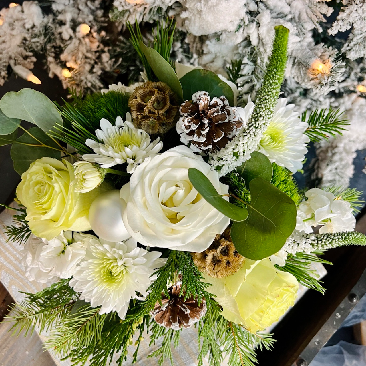 Closeup view of small white holiday arrangement with flocked tree background