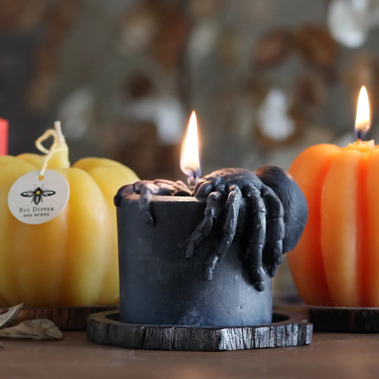 Candle with a spider design in front of pumpkins