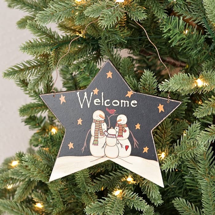 Star-shaped 'Welcome' ornament with snowmen on a Christmas tree.