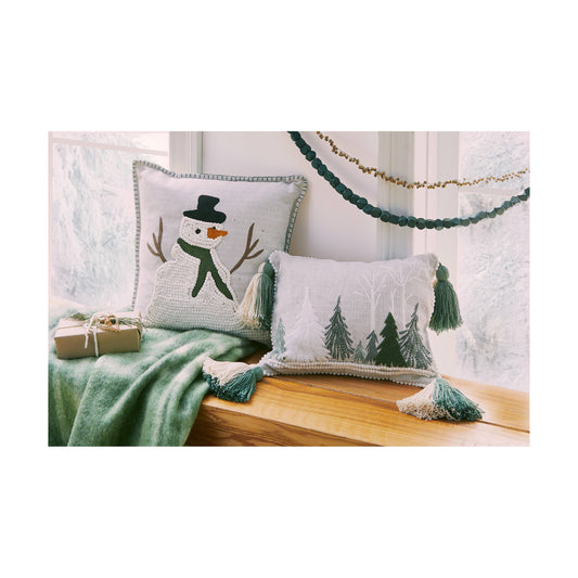Decorative pillows with winter-themed designs on a wooden surface with a green blanket and gift box.