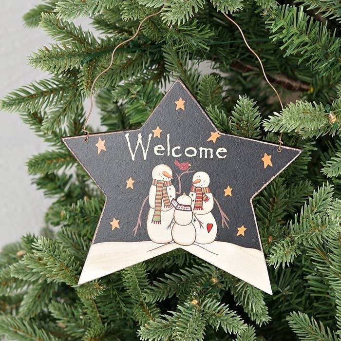 Star-shaped Christmas ornament with snowmen and 'Welcome' text on a tree.